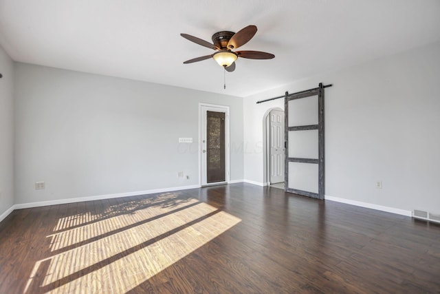 empty room featuring a barn door, ceiling fan, and dark wood-type flooring