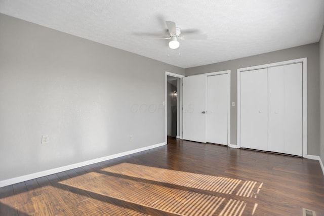 unfurnished bedroom featuring a textured ceiling, dark hardwood / wood-style floors, ceiling fan, and multiple closets