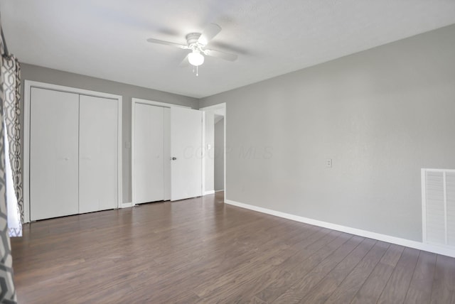 unfurnished bedroom with ceiling fan, dark wood-type flooring, and two closets