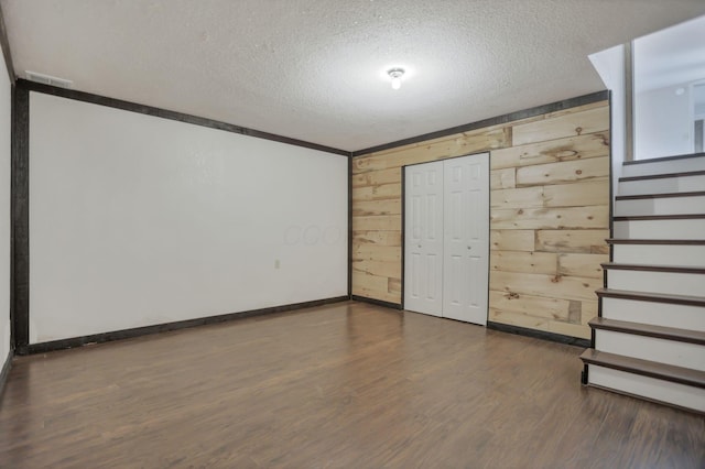 empty room featuring a textured ceiling, dark wood-type flooring, and wooden walls