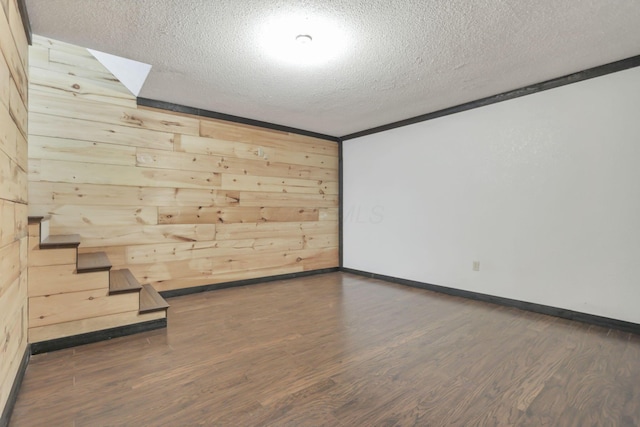 empty room with a textured ceiling, dark wood-type flooring, and wood walls