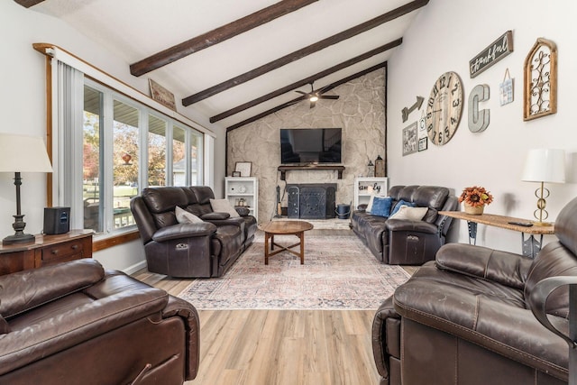 living room with vaulted ceiling with beams, ceiling fan, a stone fireplace, and light wood-type flooring