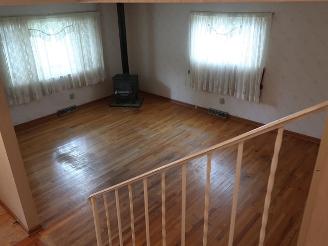 unfurnished living room featuring a wood stove, a healthy amount of sunlight, and hardwood / wood-style flooring