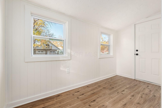 unfurnished room with wooden walls, wood-type flooring, and lofted ceiling