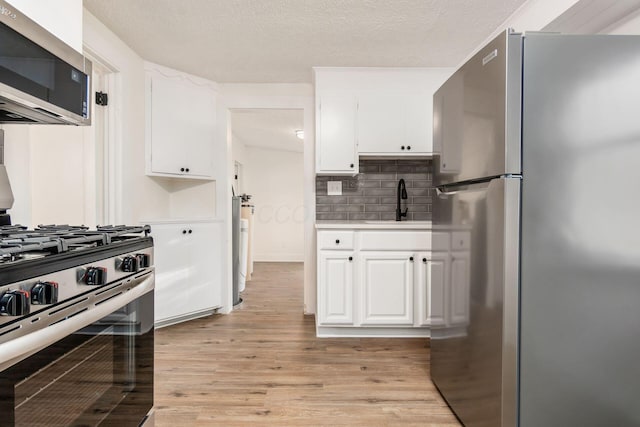 kitchen featuring white cabinets, appliances with stainless steel finishes, light wood-type flooring, and tasteful backsplash