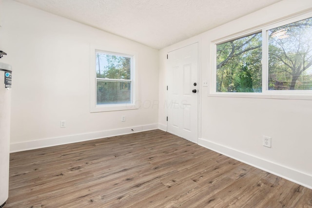 unfurnished room featuring a textured ceiling, dark wood-type flooring, and lofted ceiling