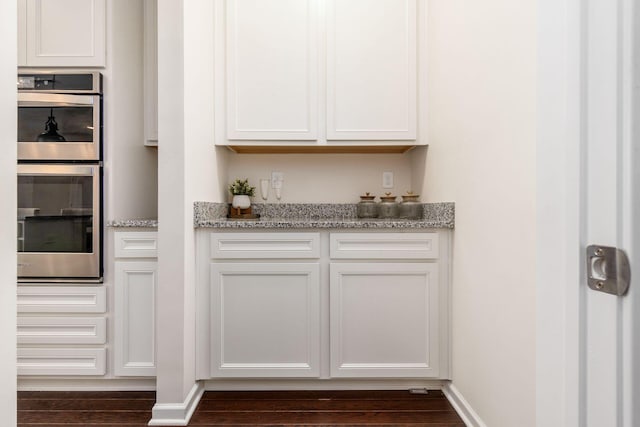 kitchen featuring dark hardwood / wood-style floors, stainless steel double oven, white cabinetry, and light stone counters