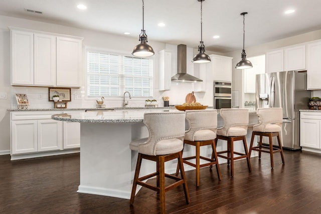 kitchen with appliances with stainless steel finishes, white cabinetry, a kitchen island, and wall chimney exhaust hood