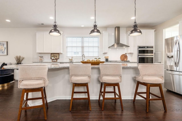 kitchen with white cabinets, wall chimney exhaust hood, stainless steel appliances, and decorative light fixtures