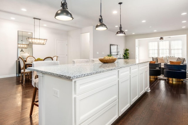 kitchen with a kitchen breakfast bar, dark hardwood / wood-style flooring, white cabinets, a kitchen island, and hanging light fixtures