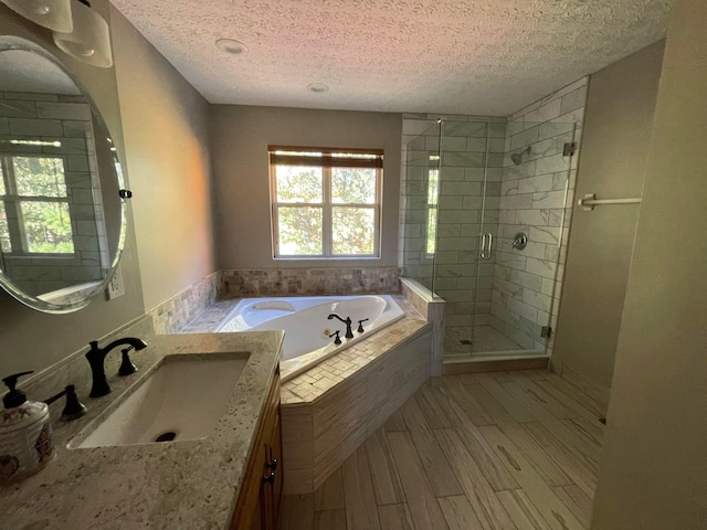 bathroom with plus walk in shower, vanity, a textured ceiling, and wood-type flooring