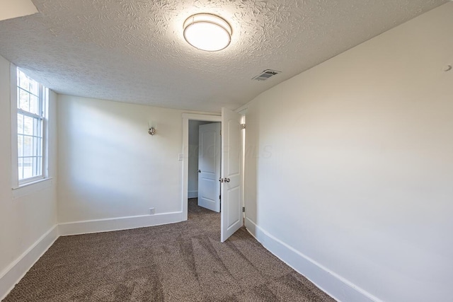 empty room with dark colored carpet and a textured ceiling