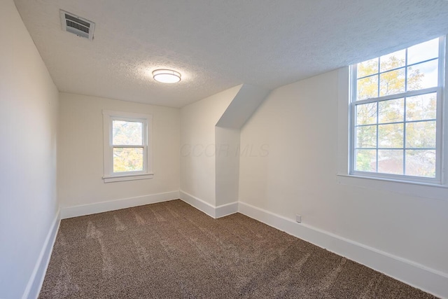 bonus room featuring a textured ceiling and dark carpet