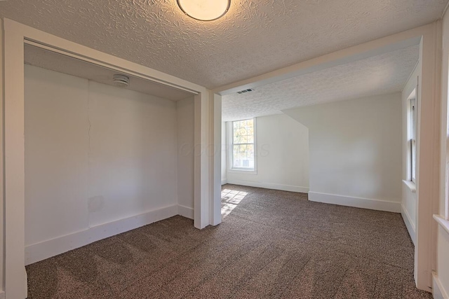 bonus room with dark colored carpet and a textured ceiling