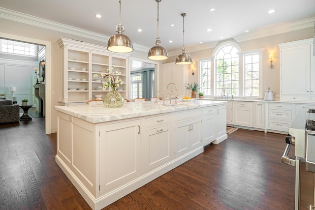 kitchen featuring hanging light fixtures, sink, white cabinets, light stone counters, and an island with sink