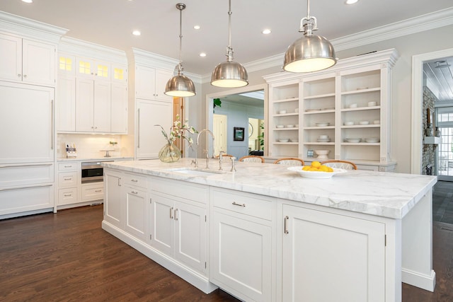 kitchen with white cabinets, decorative light fixtures, dark hardwood / wood-style flooring, an island with sink, and sink