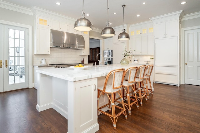 kitchen with white cabinets, hanging light fixtures, wall chimney exhaust hood, and a spacious island