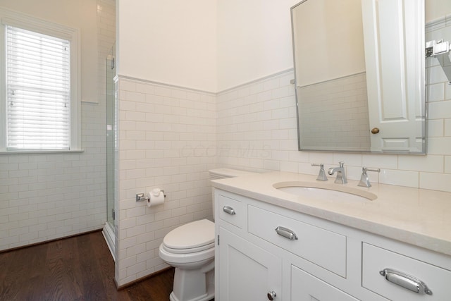 bathroom with toilet, wood-type flooring, tile walls, vanity, and a shower with door