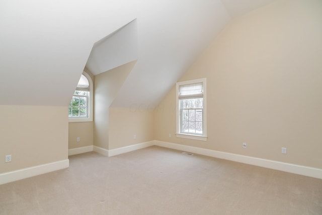 additional living space featuring plenty of natural light, light colored carpet, and vaulted ceiling