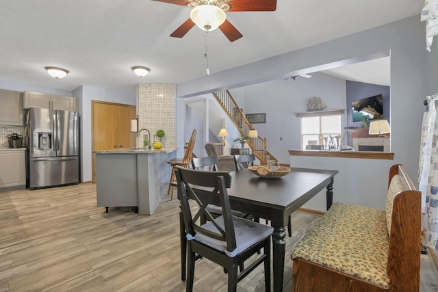 dining area featuring ceiling fan, light hardwood / wood-style floors, lofted ceiling, and a textured ceiling