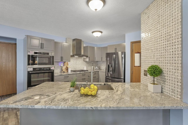 kitchen featuring hardwood / wood-style floors, gray cabinetry, wall chimney range hood, appliances with stainless steel finishes, and kitchen peninsula