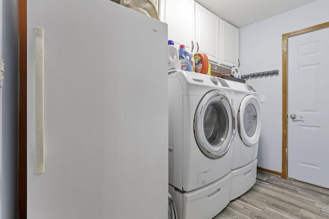 washroom with washing machine and dryer, light hardwood / wood-style flooring, cabinets, and a textured ceiling