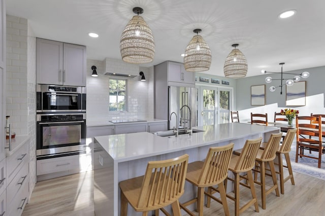 kitchen featuring a large island, gray cabinets, backsplash, hanging light fixtures, and stainless steel appliances