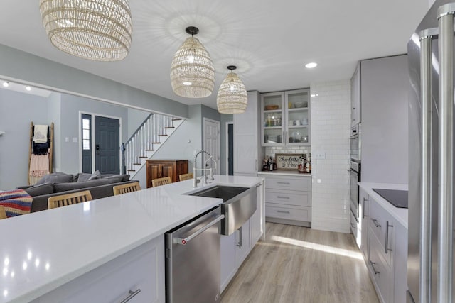 kitchen with decorative light fixtures, sink, white cabinets, light hardwood / wood-style floors, and stainless steel appliances