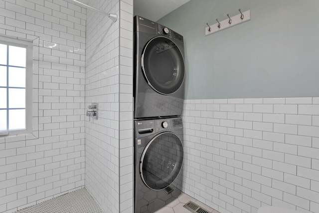 laundry room with stacked washing maching and dryer, light tile patterned floors, and tile walls