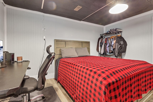 bedroom with ornamental molding, wooden walls, and light hardwood / wood-style floors