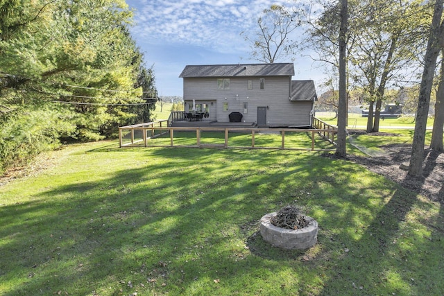 rear view of property with a wooden deck, a lawn, and an outdoor fire pit