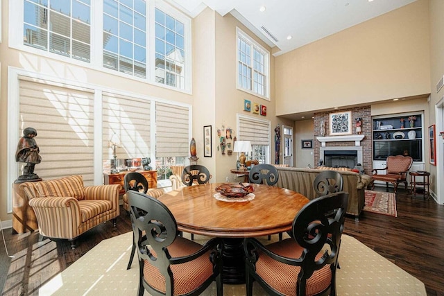 dining area featuring a high ceiling, dark hardwood / wood-style flooring, and a brick fireplace