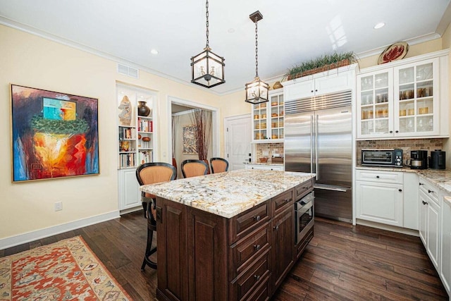 kitchen with a kitchen breakfast bar, built in appliances, a kitchen island, and dark hardwood / wood-style floors