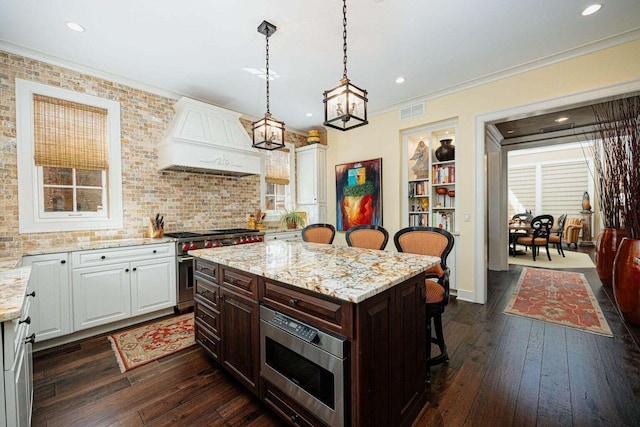 kitchen with premium range hood, a breakfast bar, stainless steel appliances, white cabinetry, and a kitchen island