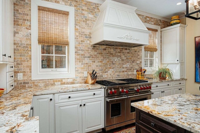 kitchen featuring white cabinets, double oven range, brick wall, and custom exhaust hood