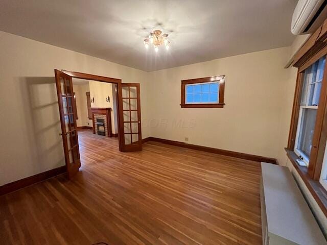 empty room featuring french doors, dark hardwood / wood-style flooring, a wealth of natural light, a wall mounted AC, and a notable chandelier