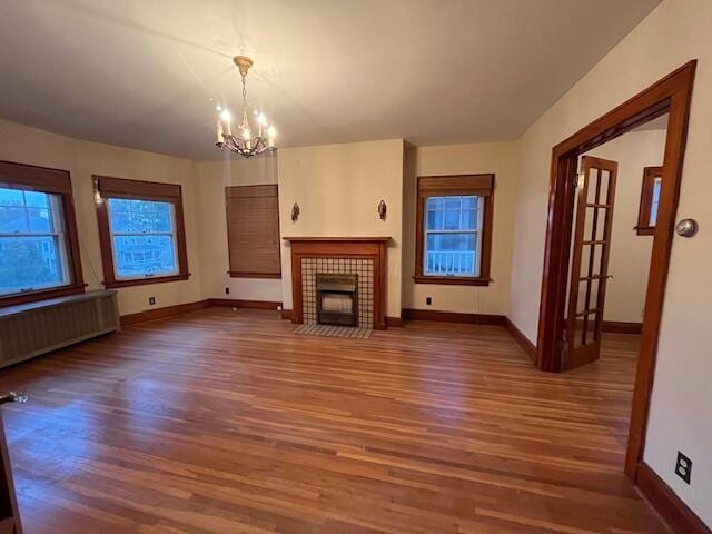 unfurnished living room with radiator, dark hardwood / wood-style flooring, a tiled fireplace, and a notable chandelier