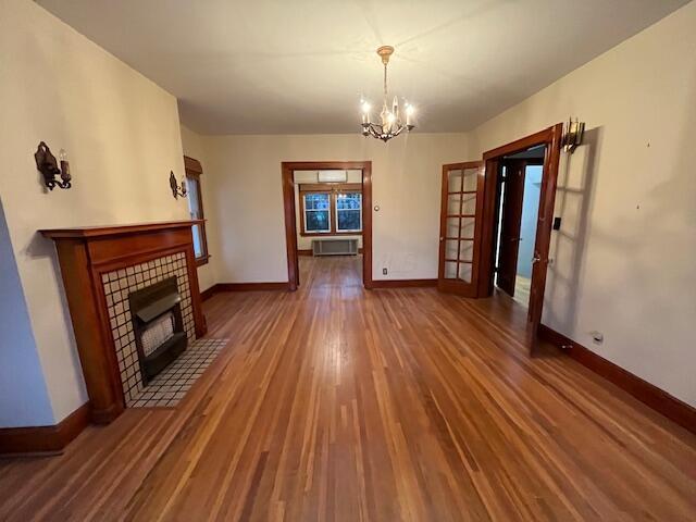 unfurnished living room featuring a tiled fireplace, french doors, dark hardwood / wood-style floors, and a notable chandelier