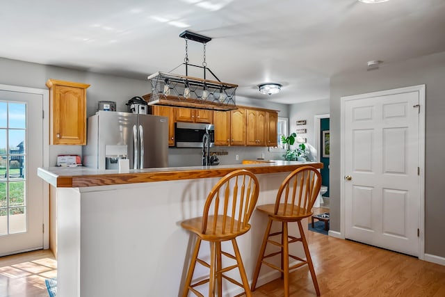 kitchen with hanging light fixtures, a notable chandelier, light hardwood / wood-style floors, kitchen peninsula, and stainless steel appliances