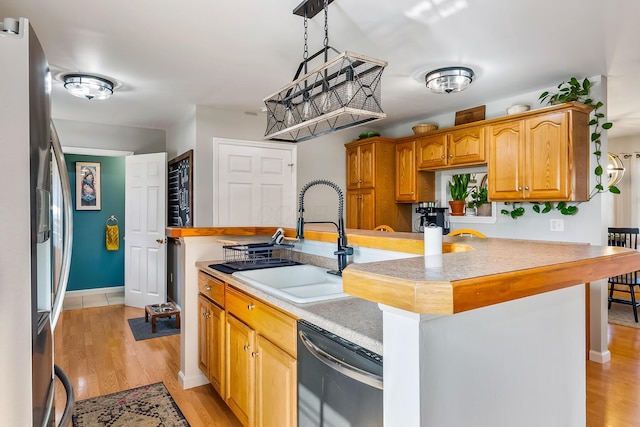 kitchen with a kitchen island with sink, sink, light wood-type flooring, appliances with stainless steel finishes, and decorative light fixtures