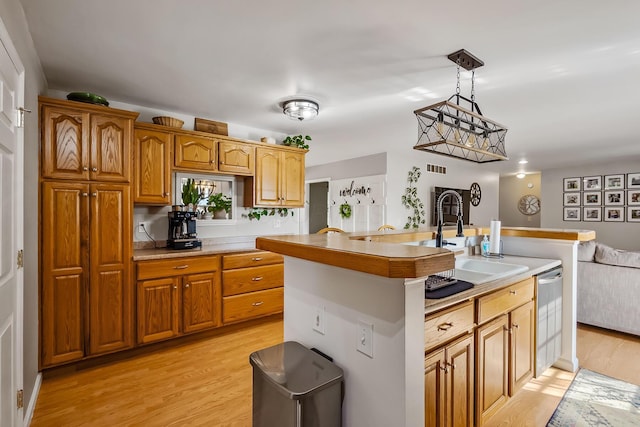 kitchen with light hardwood / wood-style floors, sink, a kitchen island with sink, and hanging light fixtures