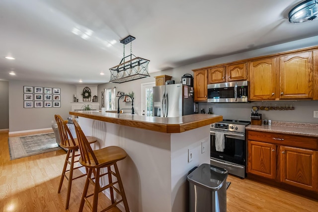 kitchen with appliances with stainless steel finishes, light hardwood / wood-style flooring, a kitchen island with sink, and pendant lighting