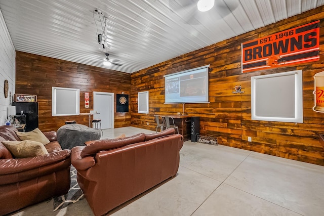 living room with ceiling fan, rail lighting, concrete floors, and wood walls