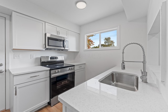 kitchen featuring light stone countertops, stainless steel appliances, sink, light hardwood / wood-style flooring, and white cabinets