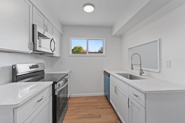 kitchen with light stone countertops, white cabinetry, sink, light hardwood / wood-style floors, and appliances with stainless steel finishes