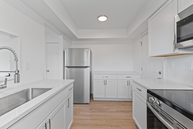 kitchen with sink, stainless steel appliances, light stone counters, white cabinets, and light wood-type flooring