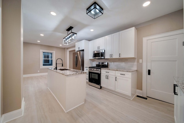 kitchen featuring light stone countertops, white cabinetry, stainless steel appliances, pendant lighting, and a kitchen island with sink