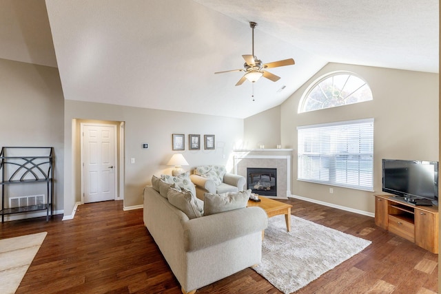 living room featuring ceiling fan, dark hardwood / wood-style floors, a tiled fireplace, and vaulted ceiling