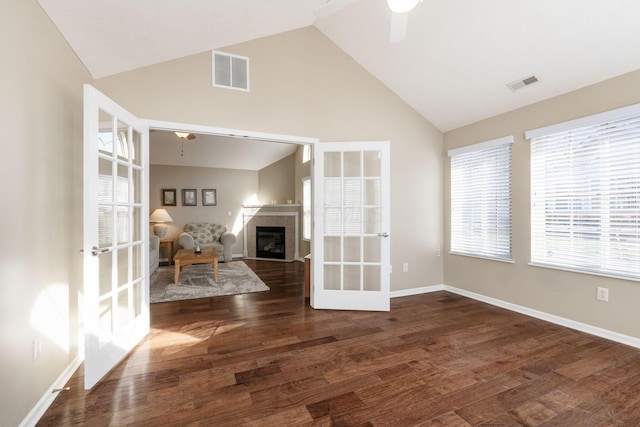 unfurnished living room featuring dark wood-type flooring, lofted ceiling, a fireplace, and french doors