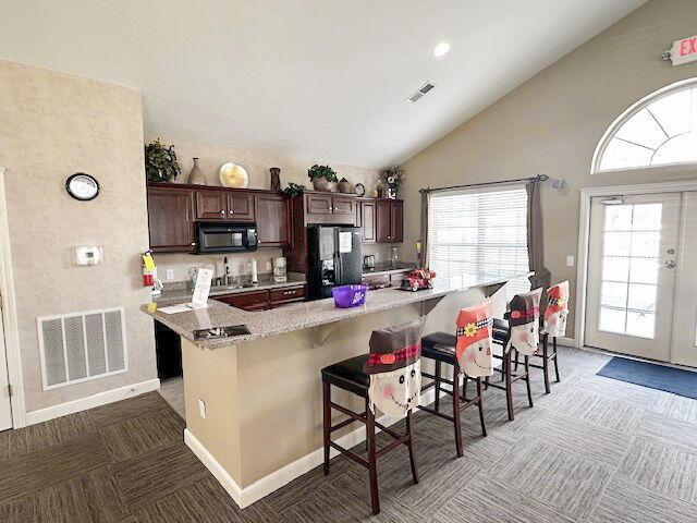 kitchen with backsplash, black appliances, a kitchen bar, dark brown cabinetry, and light stone counters